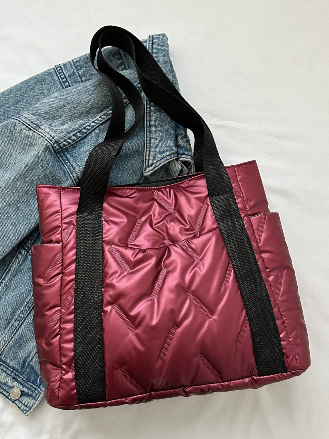 Solid color tote bag in burgundy with side pockets, displayed on a denim jacket, made of durable polyester.