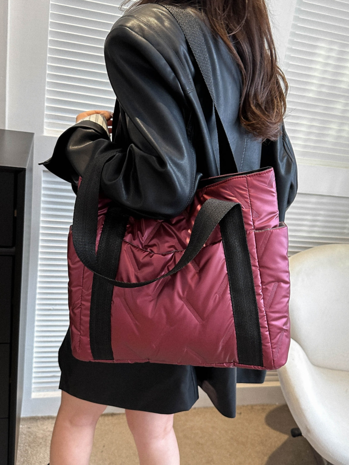 Stylish solid color tote bag with side pockets, worn over a black outfit, featuring a quilted texture and dual handles.