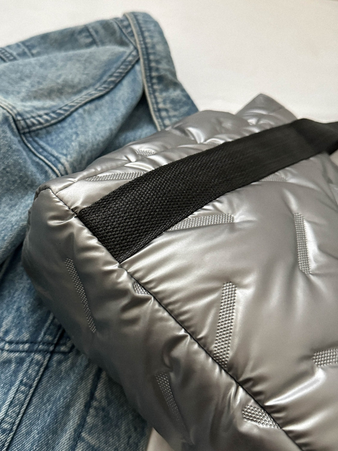 Close-up of a silver quilted tote bag next to a denim jacket, showcasing its texture and design details.