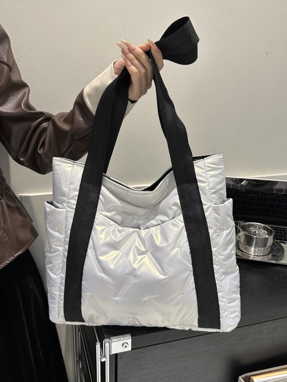 Solid color tote bag with side pockets, featuring a large size and sleek design, held by a person in fashionable attire.